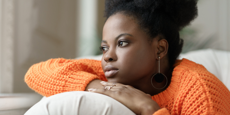 woman on brink of burnout in orange sweater, head resting on folded arm on arm of couch